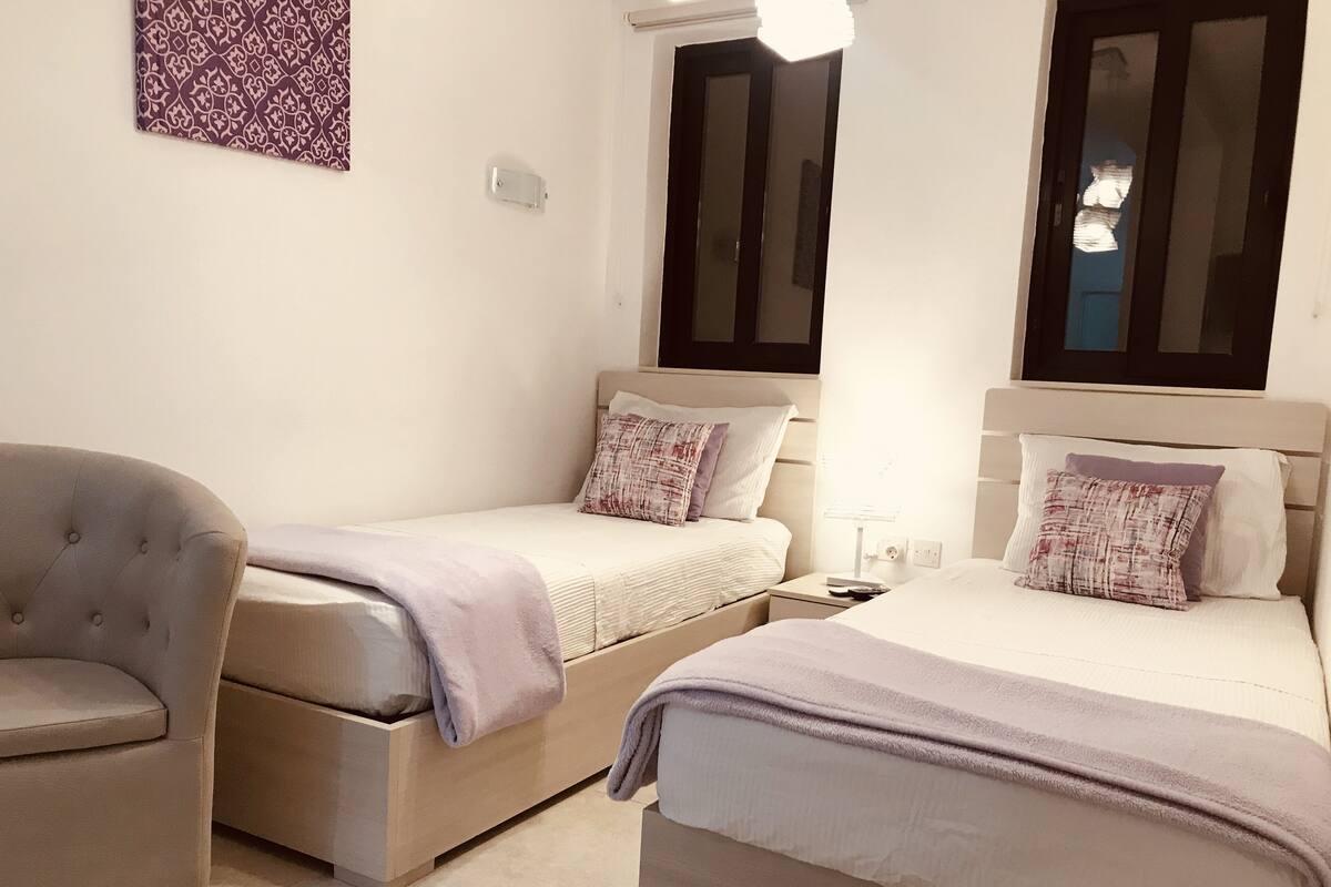Une chambre avec deux lits, une chaise et une table de chevet.