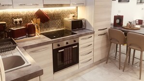 Cocina moderna con horno empotrado, microondas y estufa. Hay un comedor con dos sillas y una mesa.