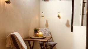 Habitación de esquina con un sillón acolchado, una mesita con una vela, y una lámpara de pared.