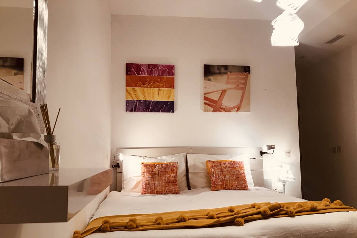 Une chambre moderne avec un grand lit, une literie blanche et deux œuvres d’art accrochées au mur.
