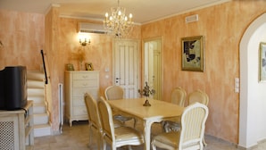 A dining room with a chandelier, a television on a stand, and a dining table with chairs. - Villa Fedra (Corfu)