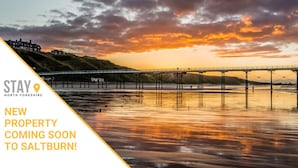 A sunset view over a coastal area with a bridge and a pier, with text indicating a new property is coming soon to Saltburn. - Caedmon Prospect (Whitby)