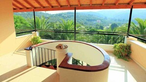 A balcony with a curved railing, a stone-tiled floor, and a view of a lush green landscape. - Cochelli Apartments (Corfu)