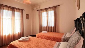 A hotel room with two beds, each with an orange quilted bedspread and pillows. There is a hanging light fixture above the beds, and the room has a simple, clean design with a picture on the wall. - Cochelli Apartments (Corfu)