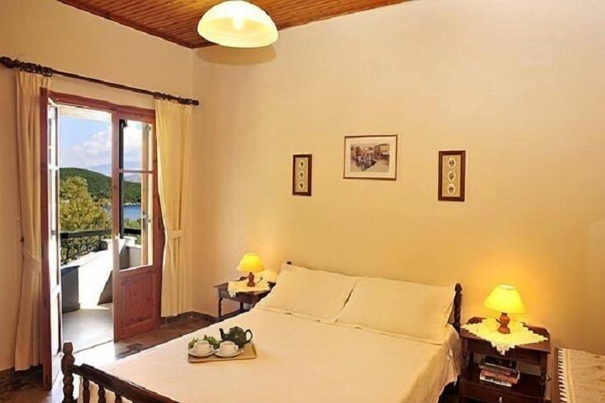 A bedroom with a bed, two bedside lamps, a window with curtains, and a view of greenery outside.