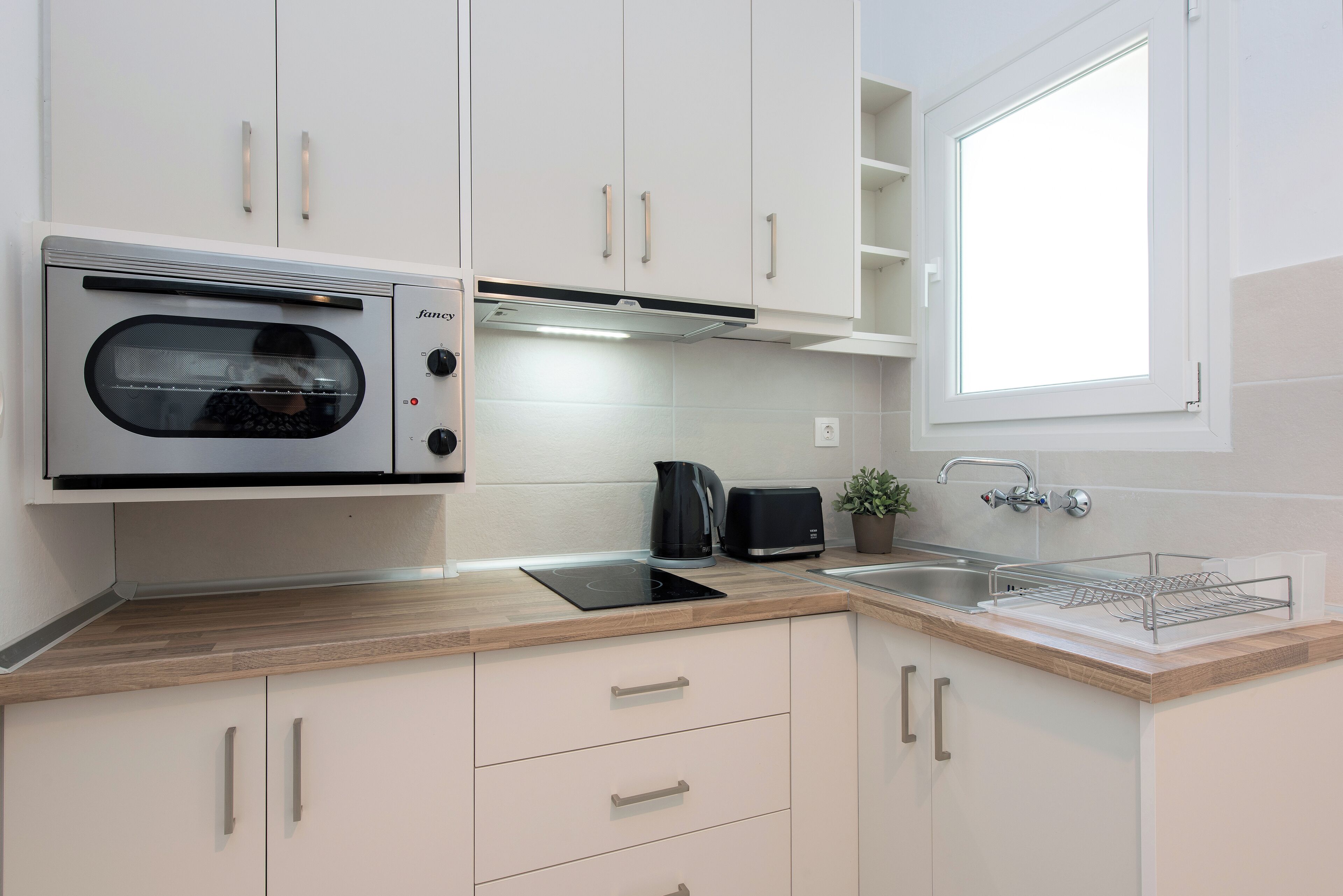 A modern kitchen with white cabinets, a built-in oven, a toaster, and a sink.