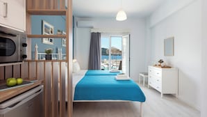 Een moderne hotelkamer met een bed, een bureau, een stoel, een kitchenette en uitzicht op zee door het raam.