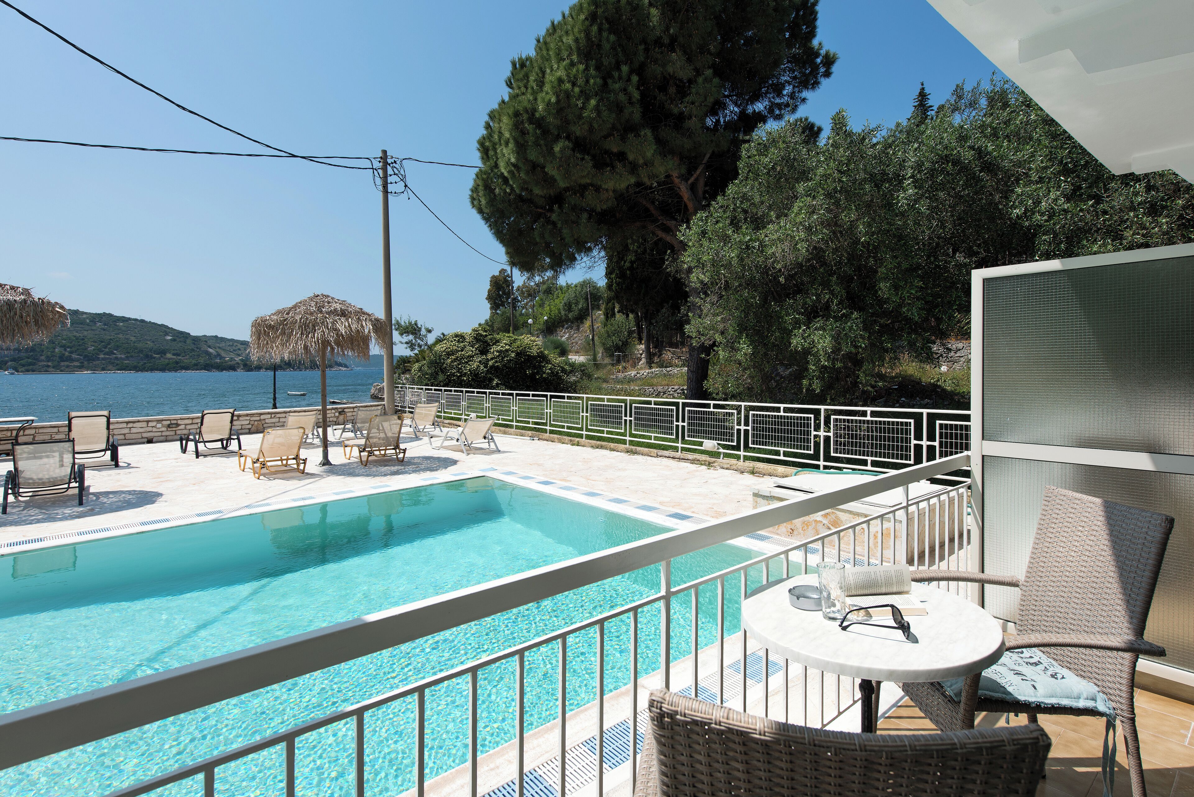 Un espace piscine aménagé avec des chaises longues et une table, offrant une vue sur un plan d’eau et des collines.