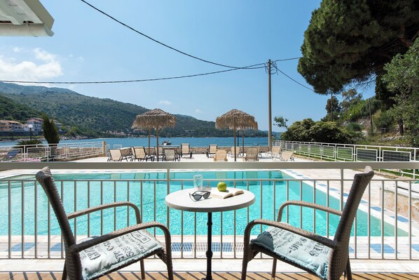 A pool area with wicker chairs and a table, overlooking a body of water and hills.
