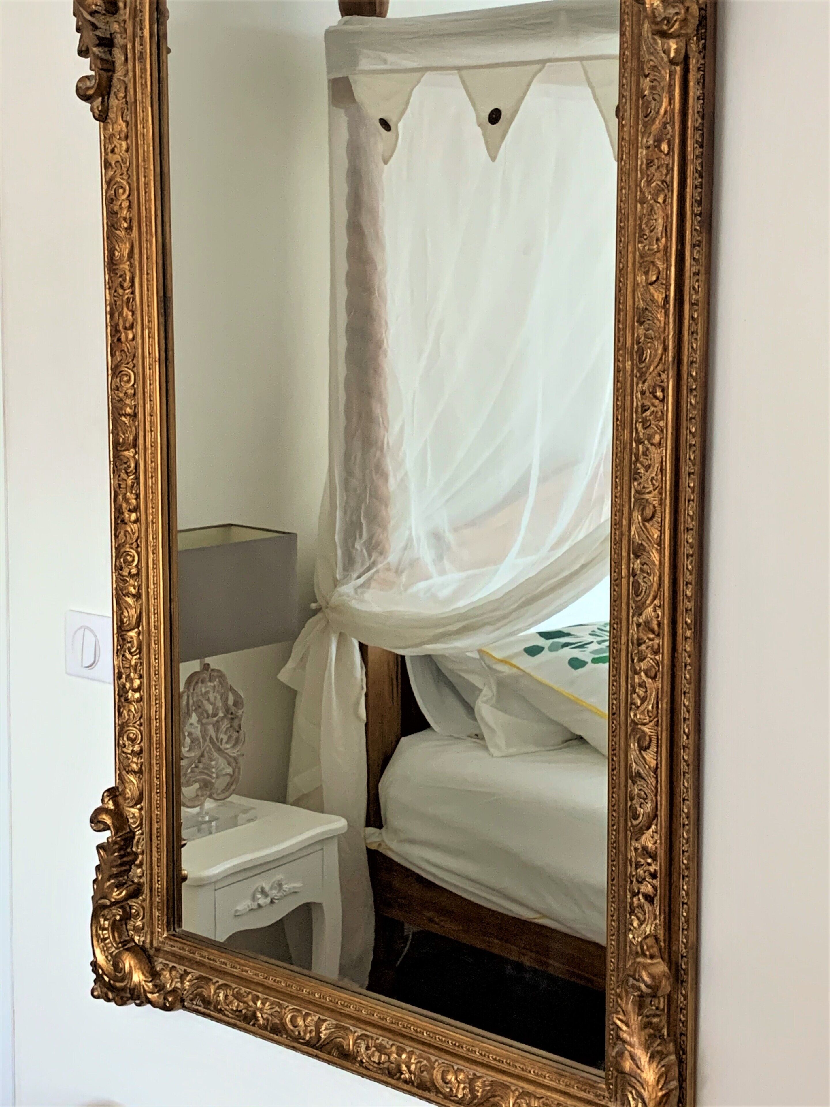 A bedroom with a four-poster bed, a nightstand, and a mirror with an ornate frame.