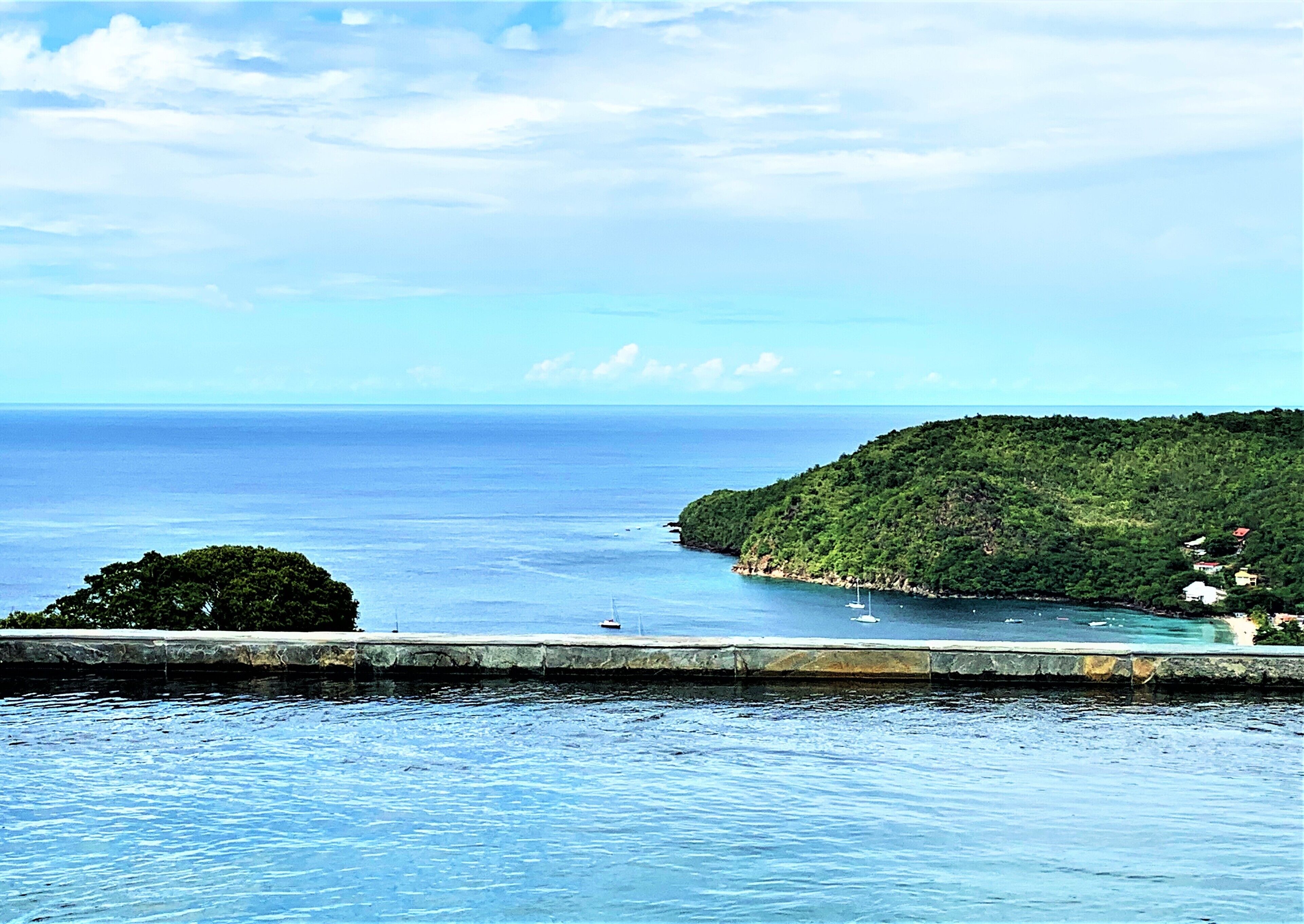 Un paisaje costero con vista despejada al mar, una pequeña isla de vegetación exuberante y algunas embarcaciones.