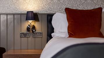 A hotel room with a bed, a nightstand with a lamp, and a wall with a floral pattern.