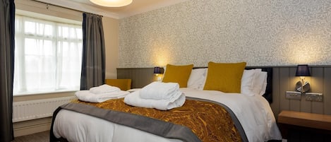 A hotel room with a large bed, two bedside lamps, a window with curtains, and a patterned wallpaper.