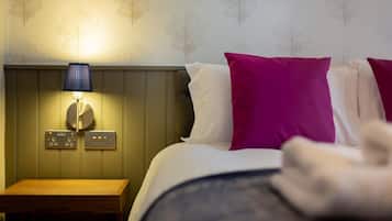 Habitación de hotel con cama, mesita de noche con lámpara y pared con motivos de hojas.