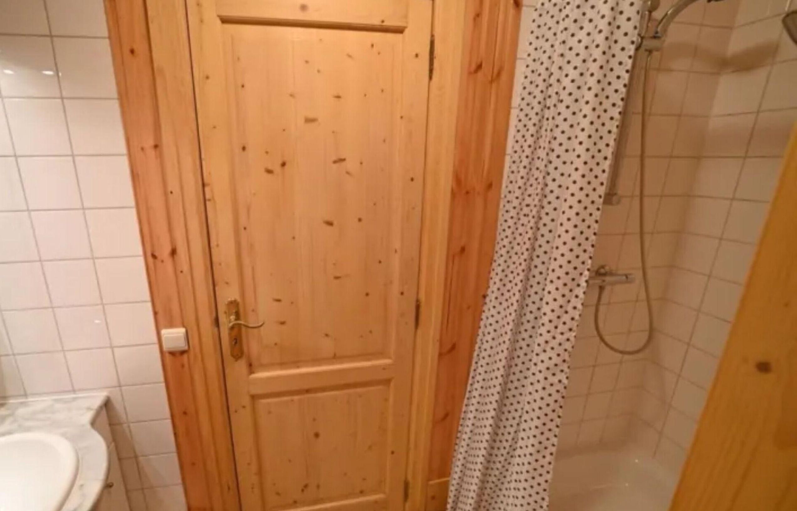Une porte en bois, une douche avec un rideau à pois et un mur carrelé.