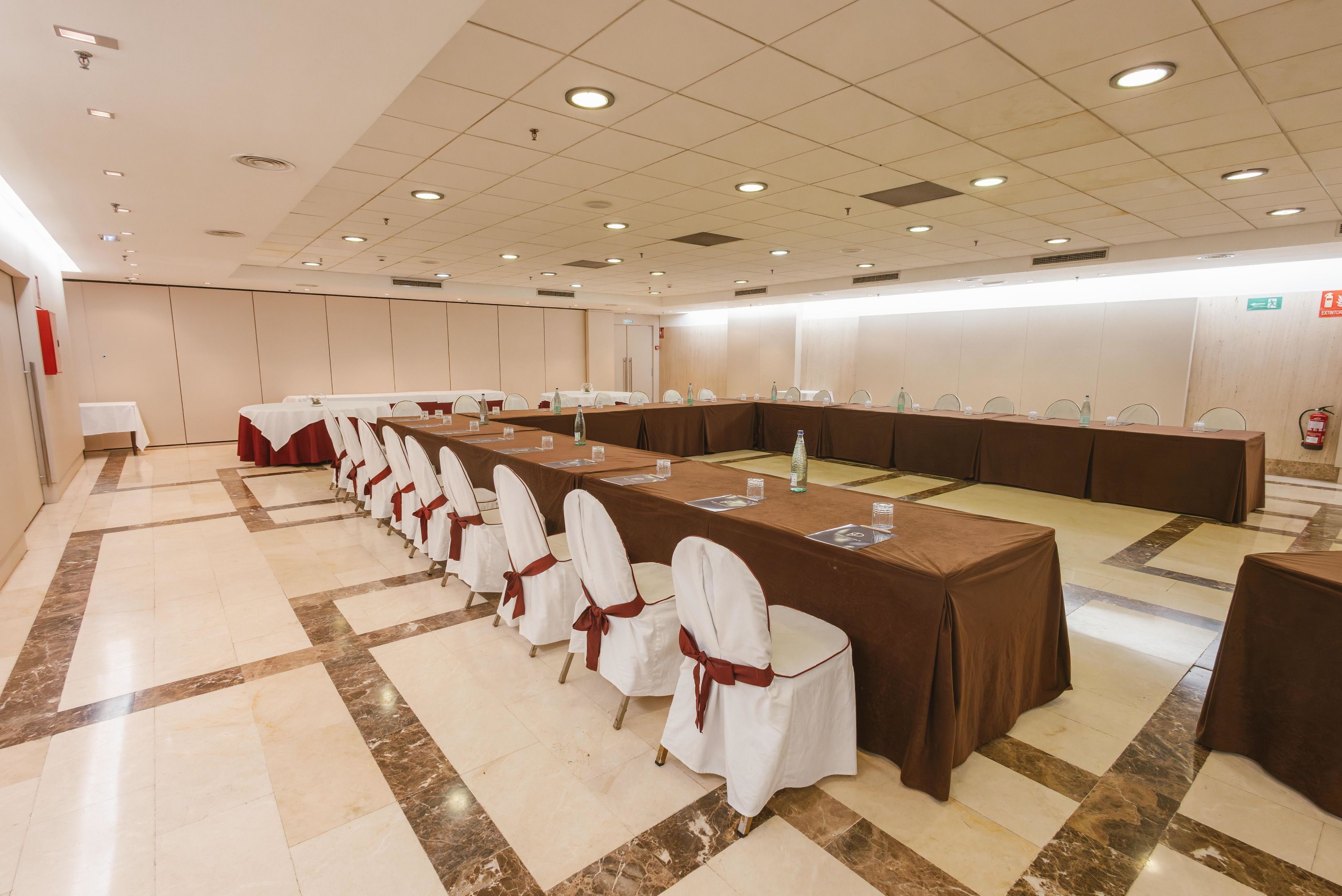 A conference room with long tables, chairs, and a tiled floor.