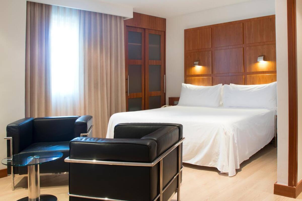 Een hotelkamer met een bed, bureau, stoel en een groot raam met gordijnen.