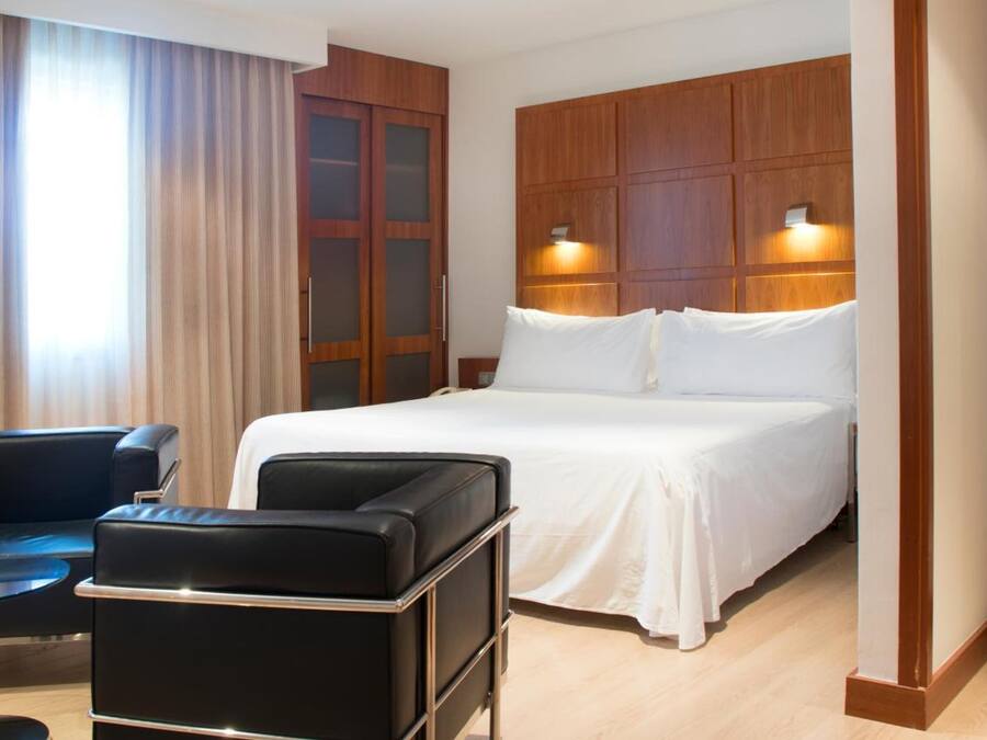 A hotel room with a bed, a desk, a chair, and a large window with curtains.