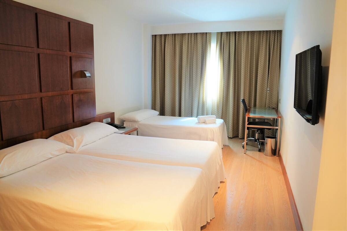 Een hotelkamer met twee bedden, een houten hoofdeinde, een televisie en een bureau met stoel.
