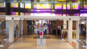 Een moderne lobby met een centraal receptiebalie, een beeld en een decoratieve bloemstelling.