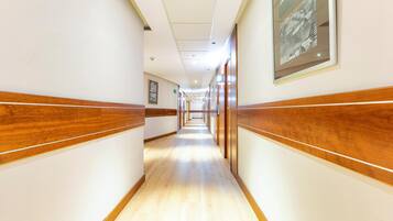A hotel corridor with wooden paneling, framed pictures on the walls, and a light-colored floor.