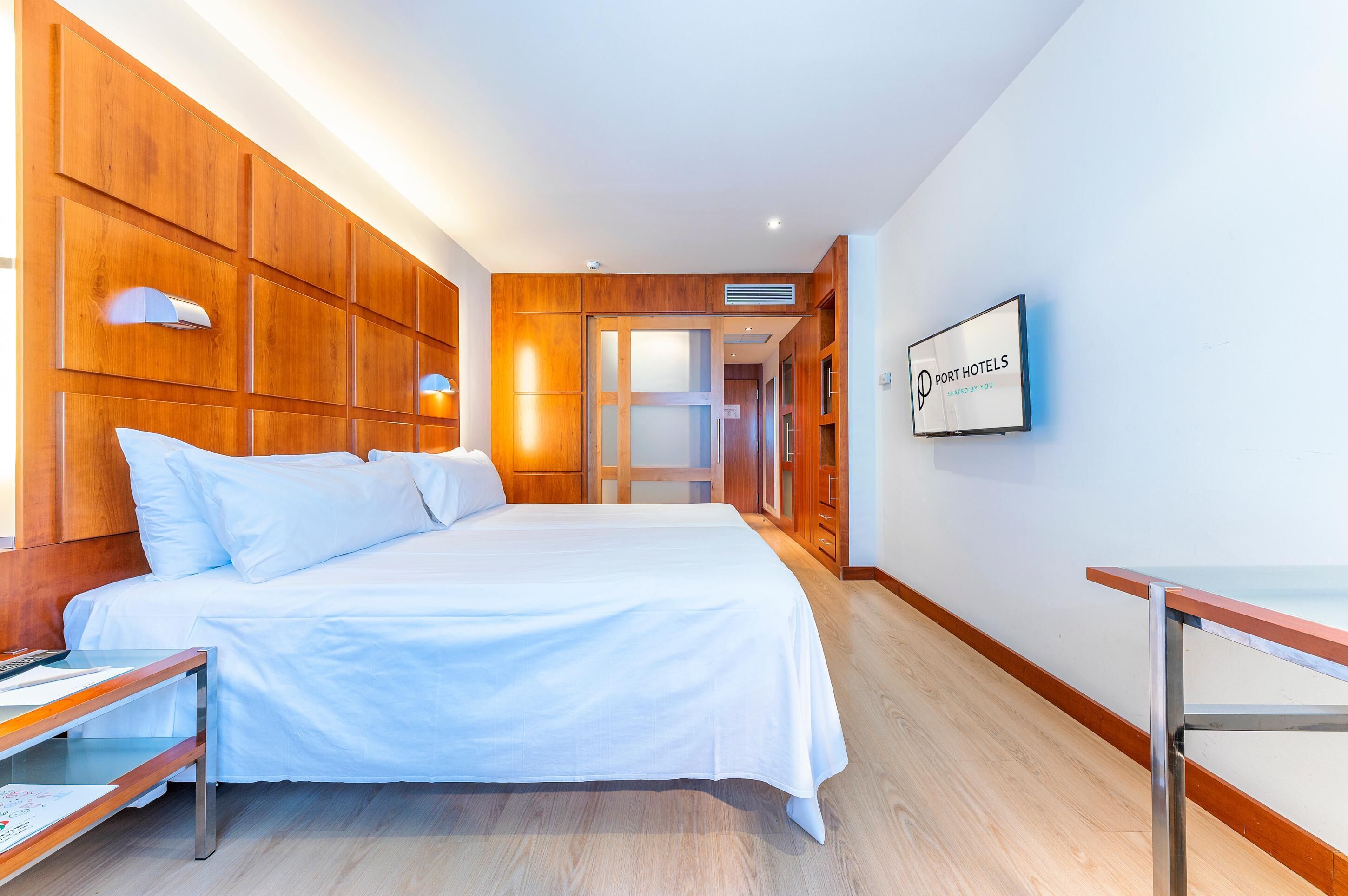 Ein Hotelzimmer mit einem großen Bett, Holzvertäfelung an den Wänden, einem an der Wand montierten Fernseher und Blick auf den Strand durch das Fenster.