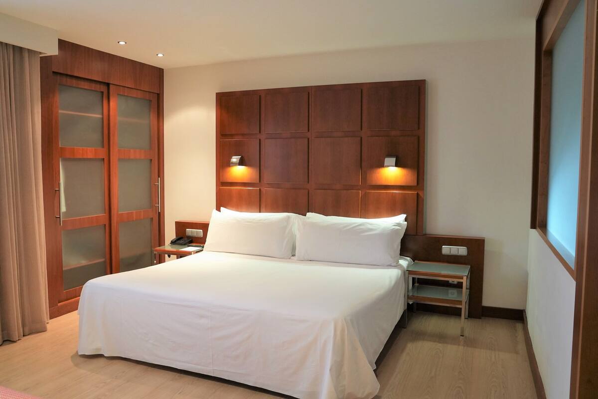 Hotelkamer met een groot bed, houten hoofdeinde, twee nachtkastjes en een garderobe met ruiten van geëtst glas.