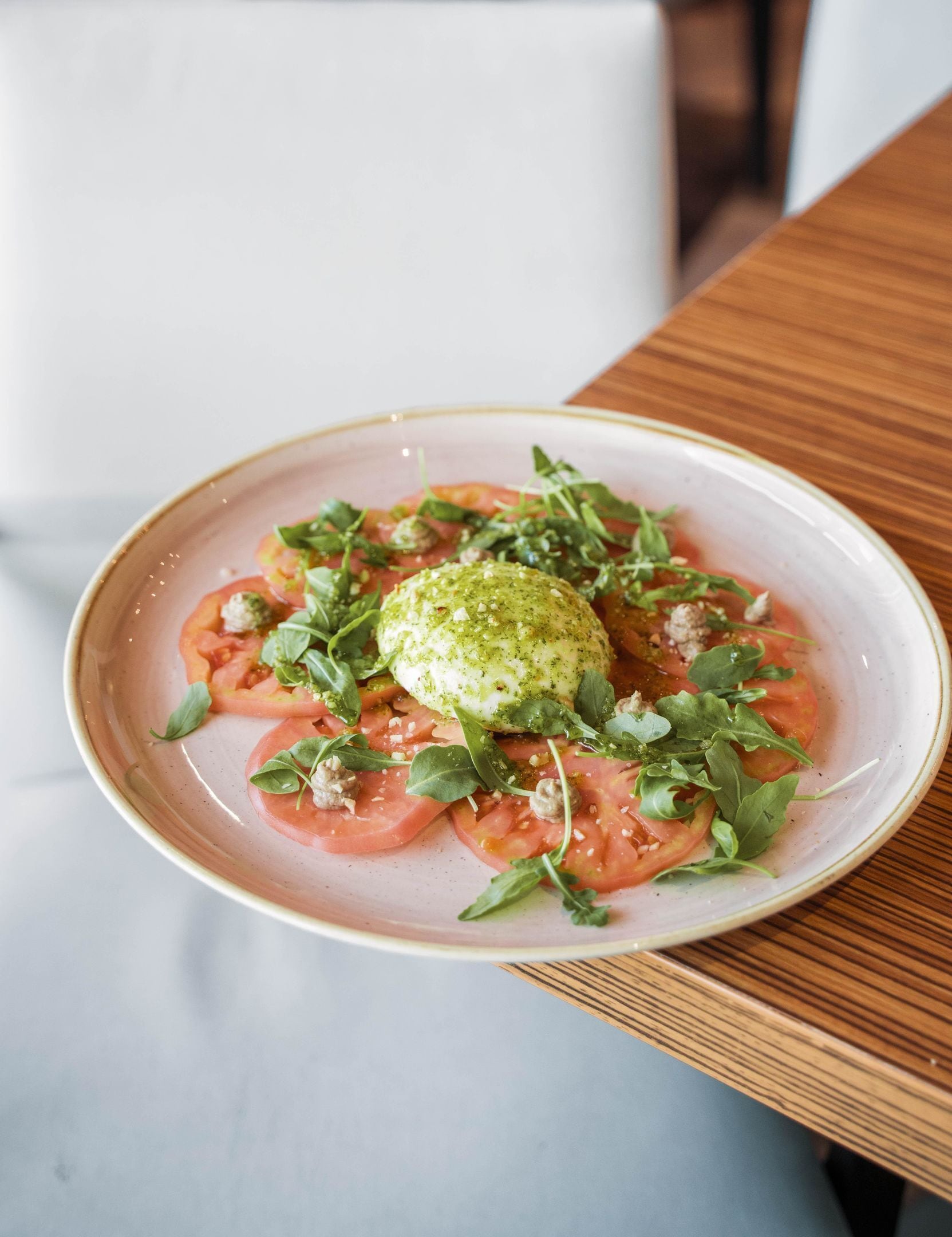 Une assiette de nourriture garnie d’une sauce verte, de tranches de tomates et de légumes verts, le tout présenté sur une assiette en céramique.