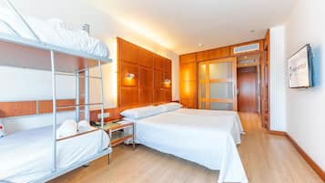 Ein Hotelzimmer mit Etagenbetten, einem Holzschrank, einem Schreibtisch mit Stuhl und einem an der Wand montierten Fernseher.