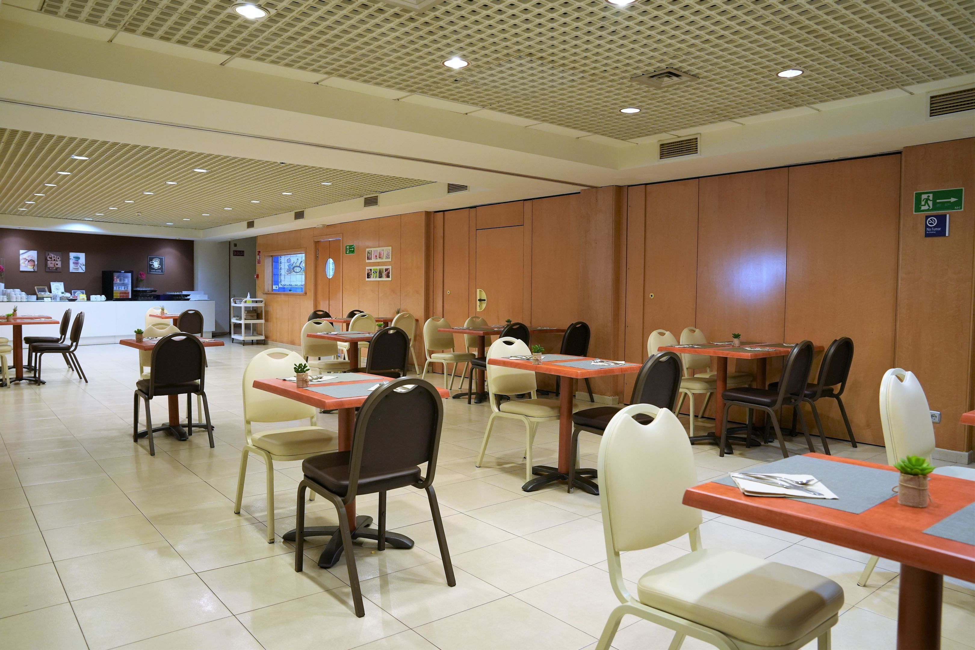 A spacious dining area with multiple tables and chairs, a reception desk, and a bulletin board with notices.