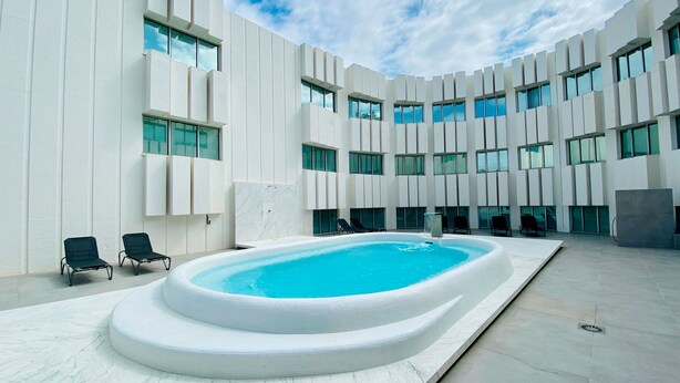 Een modern gebouw met een centraal gelegen zwembad, meerdere ramen en lounge stoelen.