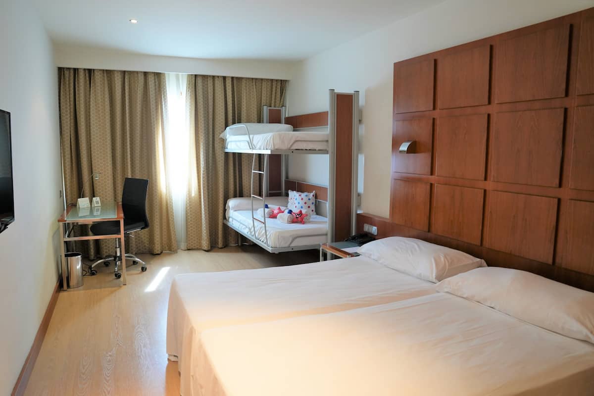 Een hotelkamer met twee bedden, een bureau met stoel, een televisie en een groot raam met gordijnen.