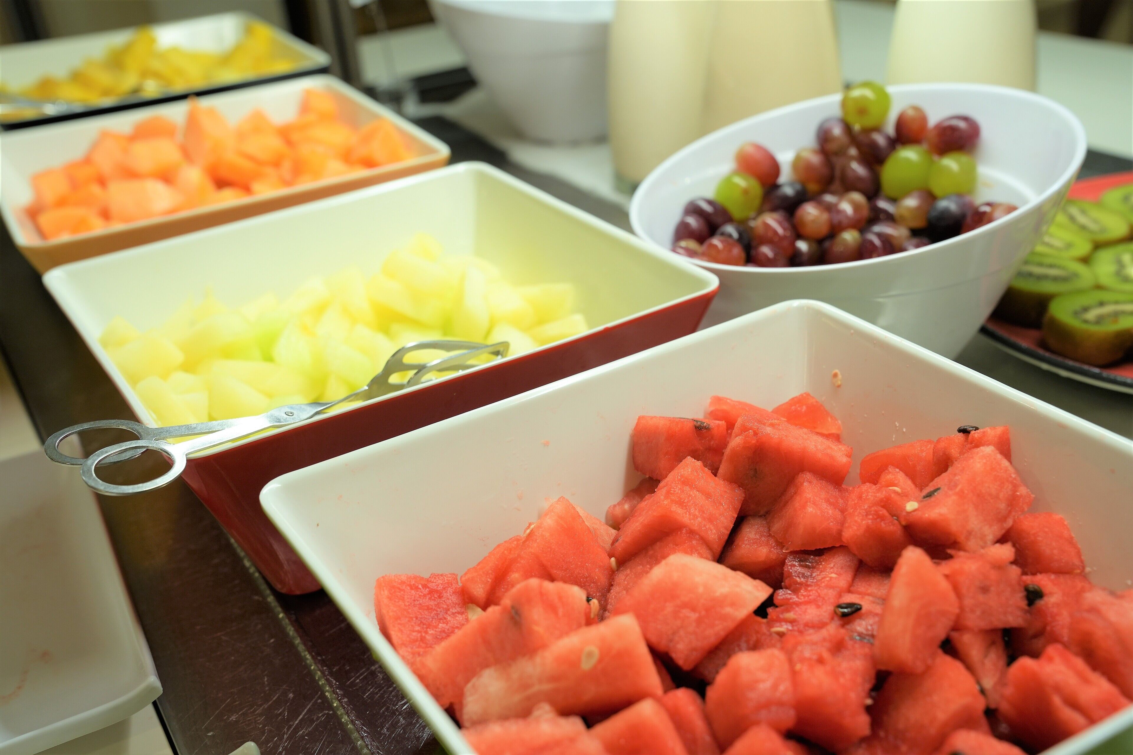 Une table de buffet proposant une variété de fruits, notamment des pastèques, des ananas et des raisins.