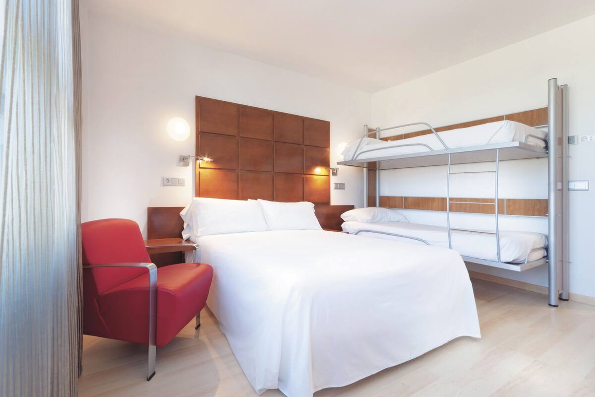Een hotelkamer met een stapelbed, een rode stoel, een nachtkastje en een wandlamp.