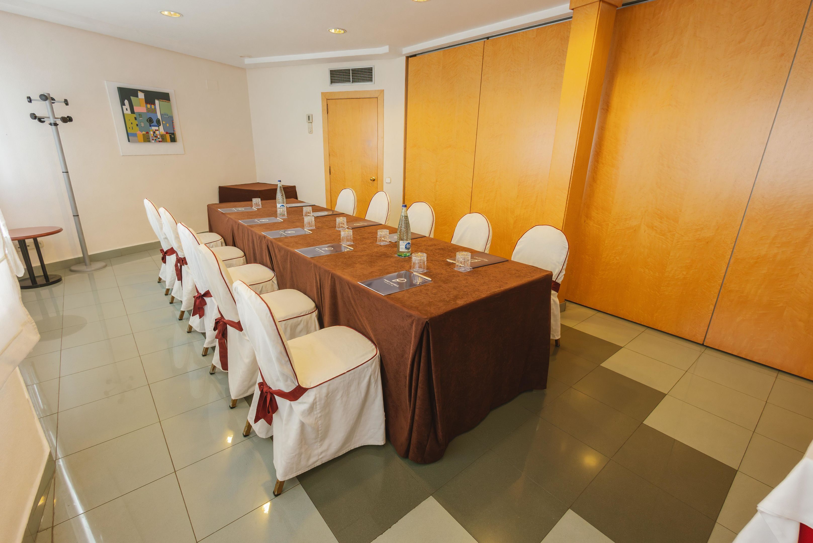 Une salle de conférence avec une longue table, des chaises blanches ornées de rubans rouges, et une porte en bois à l’arrière-plan.