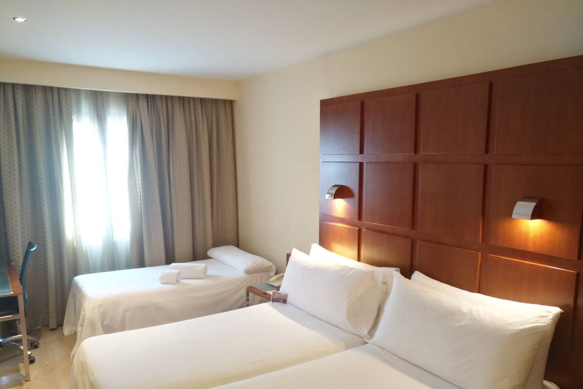 Een hotelkamer met twee enkele bedden, een houten hoofdeinde, een bureau en een stoel.