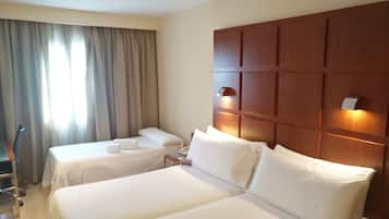 Habitación de hotel con dos camas individuales, un cabecero de madera, un escritorio y una silla.