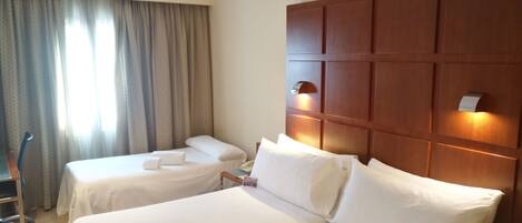 A hotel room with two single beds, a wooden headboard, a desk, and a chair.