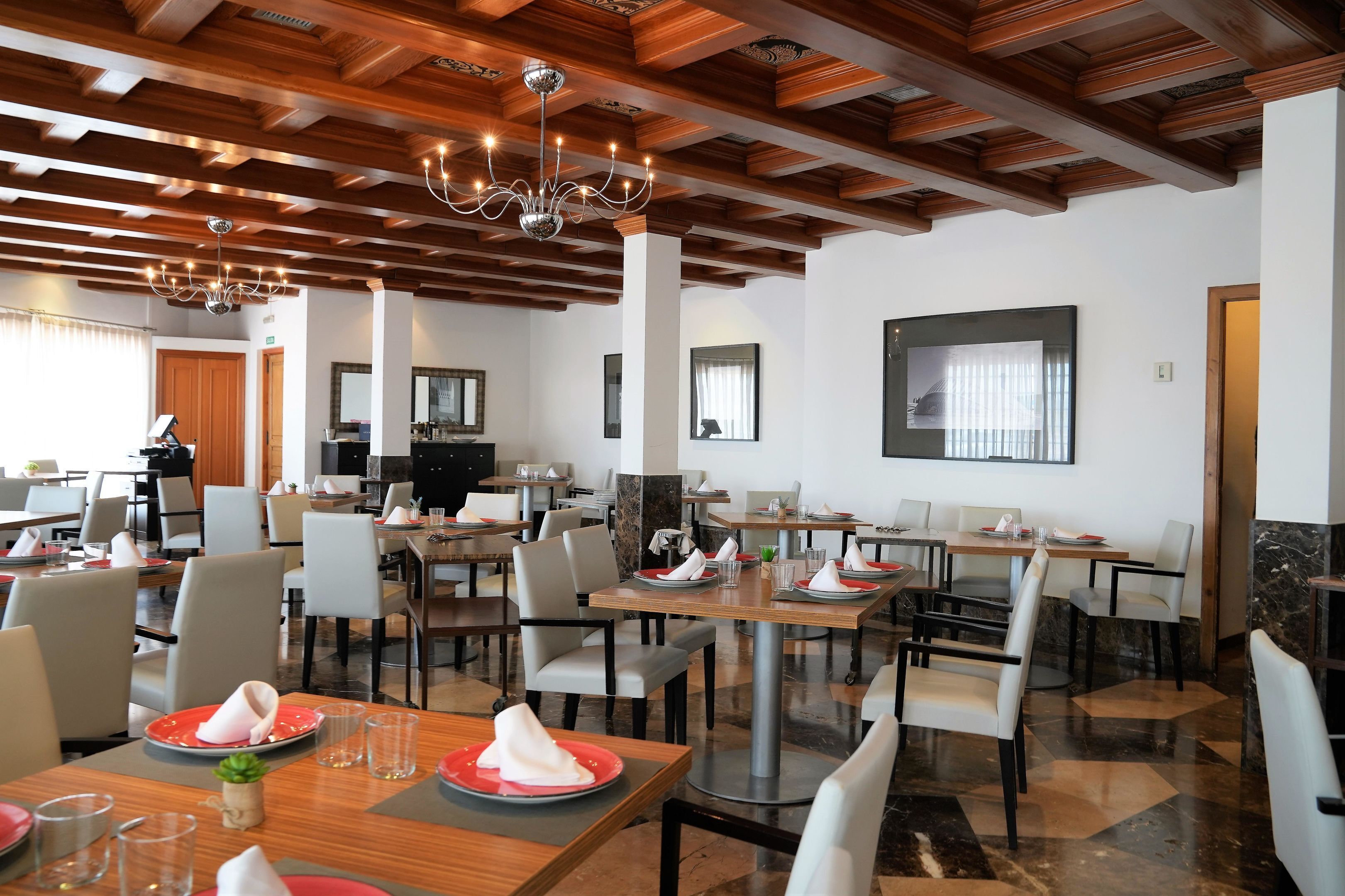 Un'ampia sala da pranzo con travi in legno e un lampadario, con tavoli apparecchiati con piatti e bicchieri.