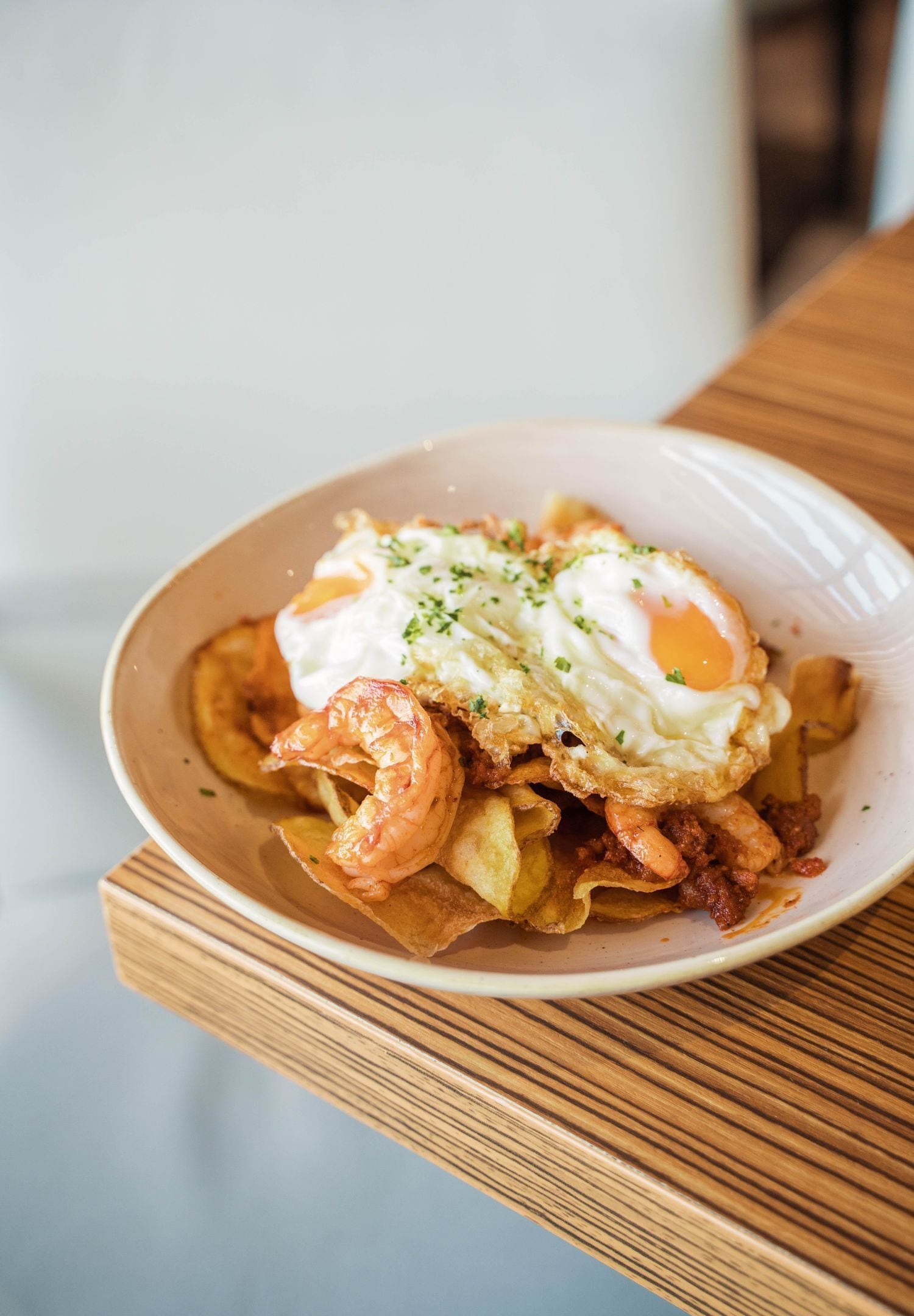 A bowl of food with a fried egg, shrimp, and a dollop of sauce on a wooden table.