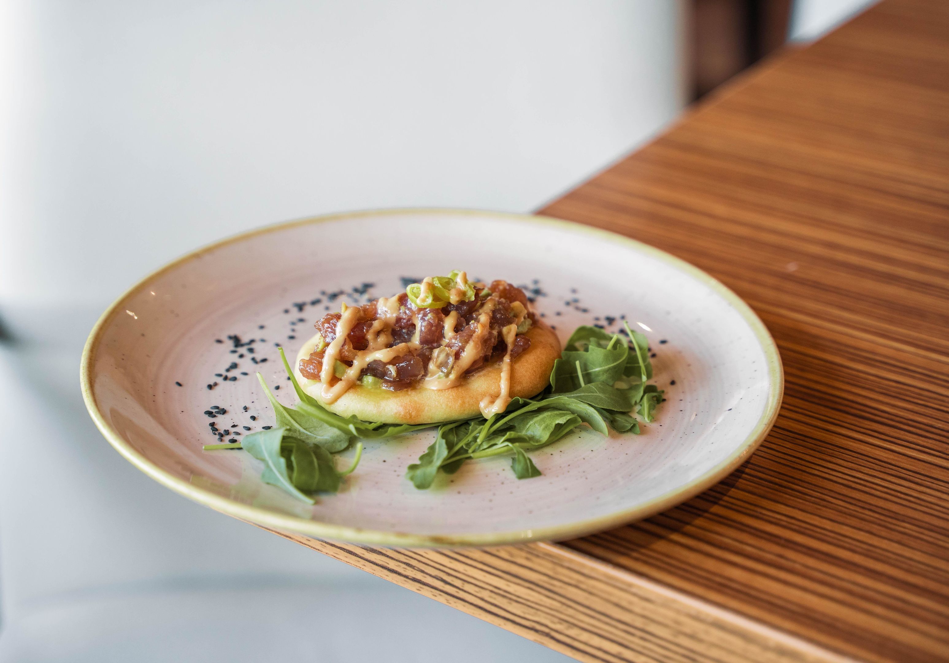 A plate with a food item, greens, and black seeds on a table.