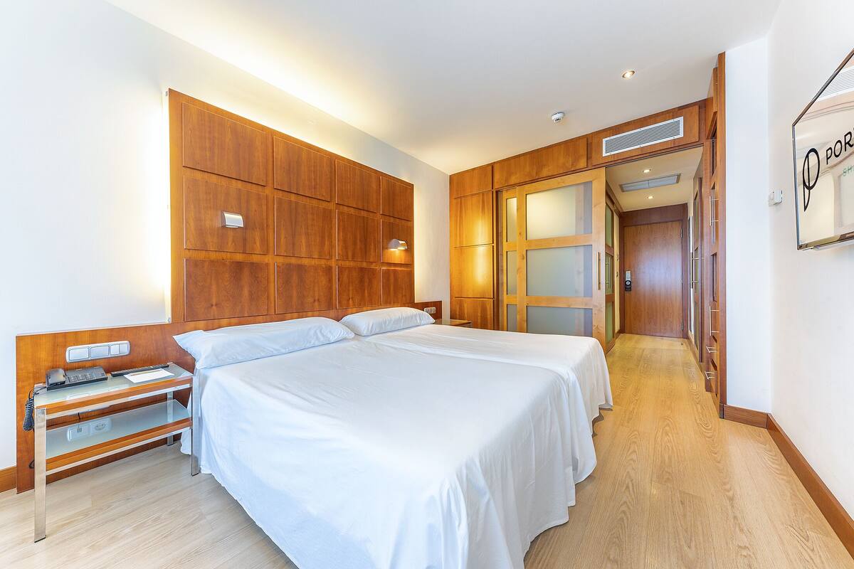 Een hotelkamer met een houten hoofdeinde, een bureau met telefoon, en een bed met wit beddengoed.
