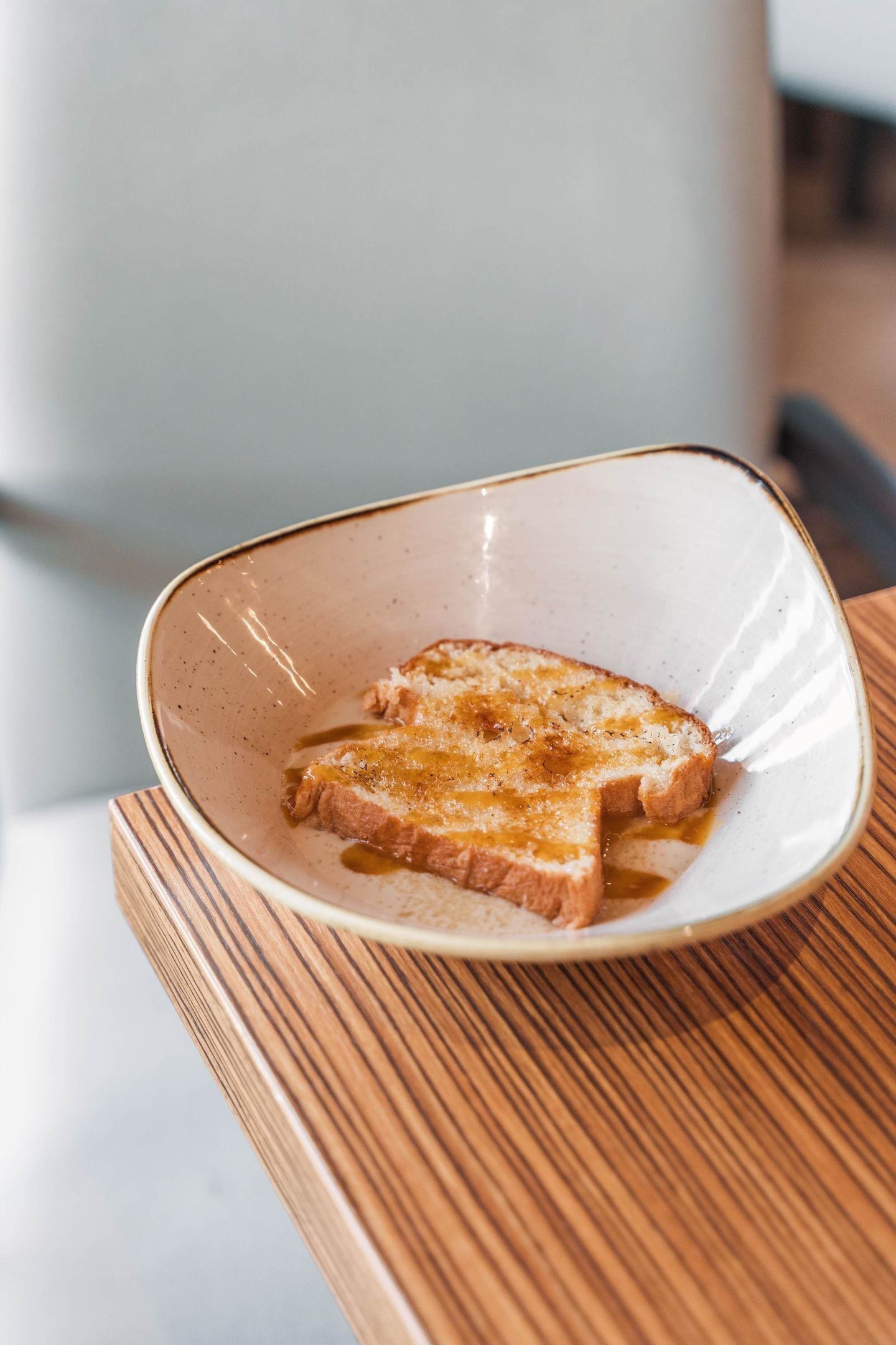 Una rebanada de tostada con mantequilla sobre un plato de cerámica en una mesa de madera.