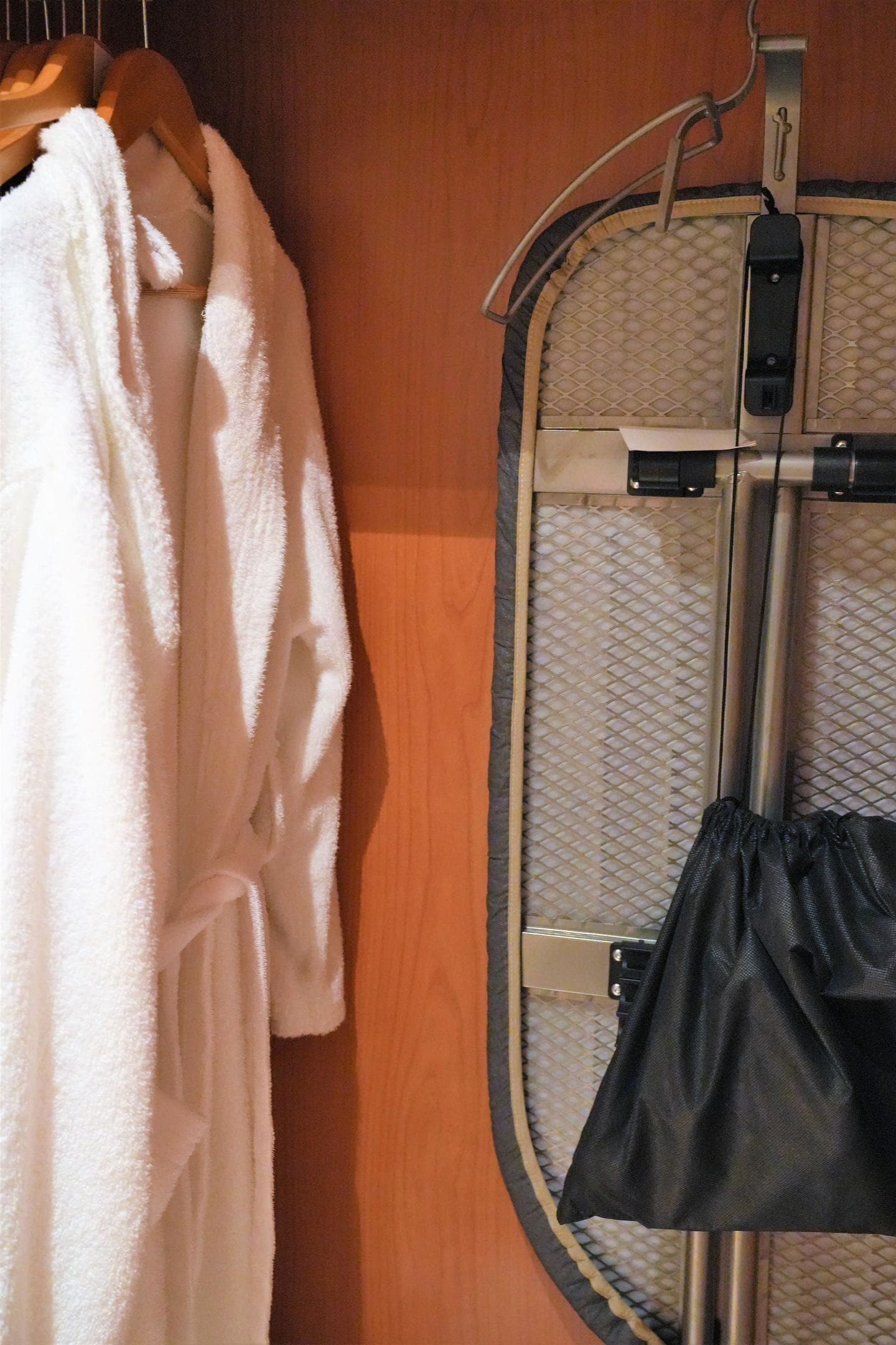 A wooden wall with a metal ironing board and a white robe hanging on a wooden hanger.