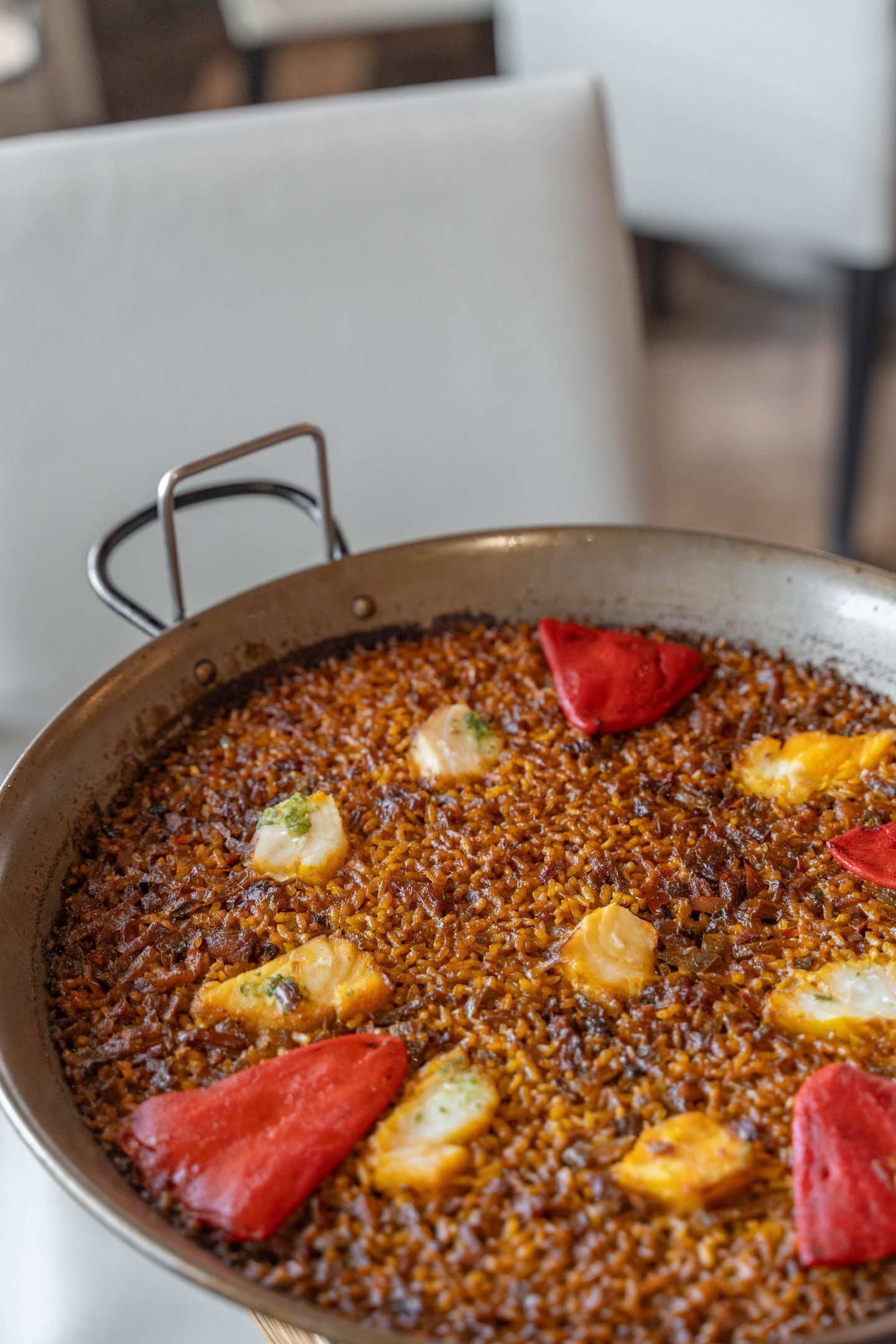 Une grande poêle remplie d’un plat composé de riz, de morceaux de poisson et de piments rouges.