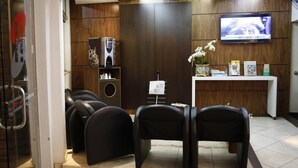 Un espace d’accueil avec un téléviseur, un comptoir de réception et plusieurs chaises noires.