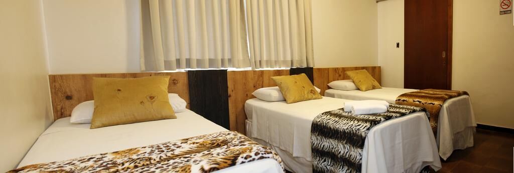 A hotel room with two single beds, each with a wooden headboard, white bedding, and a leopard print blanket.