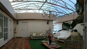 Un espace intérieur spacieux avec un plafond haut et un toit en verre, comprenant un canapé, une table basse avec des magazines et un berceau.