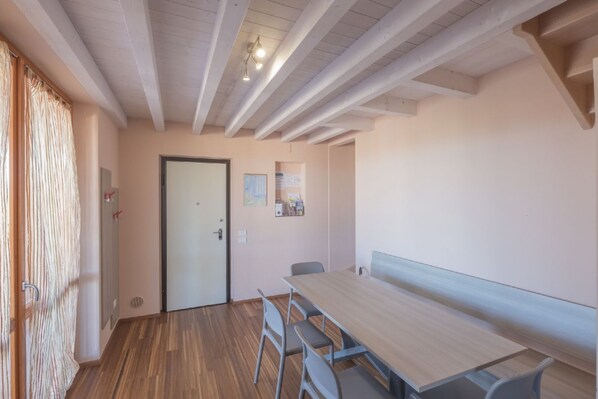 A room with a wooden floor, a long table with chairs, a door, and a light fixture on the ceiling.