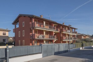 Un edificio residencial de varios pisos con balcones, una entrada con reja y un cielo despejado.